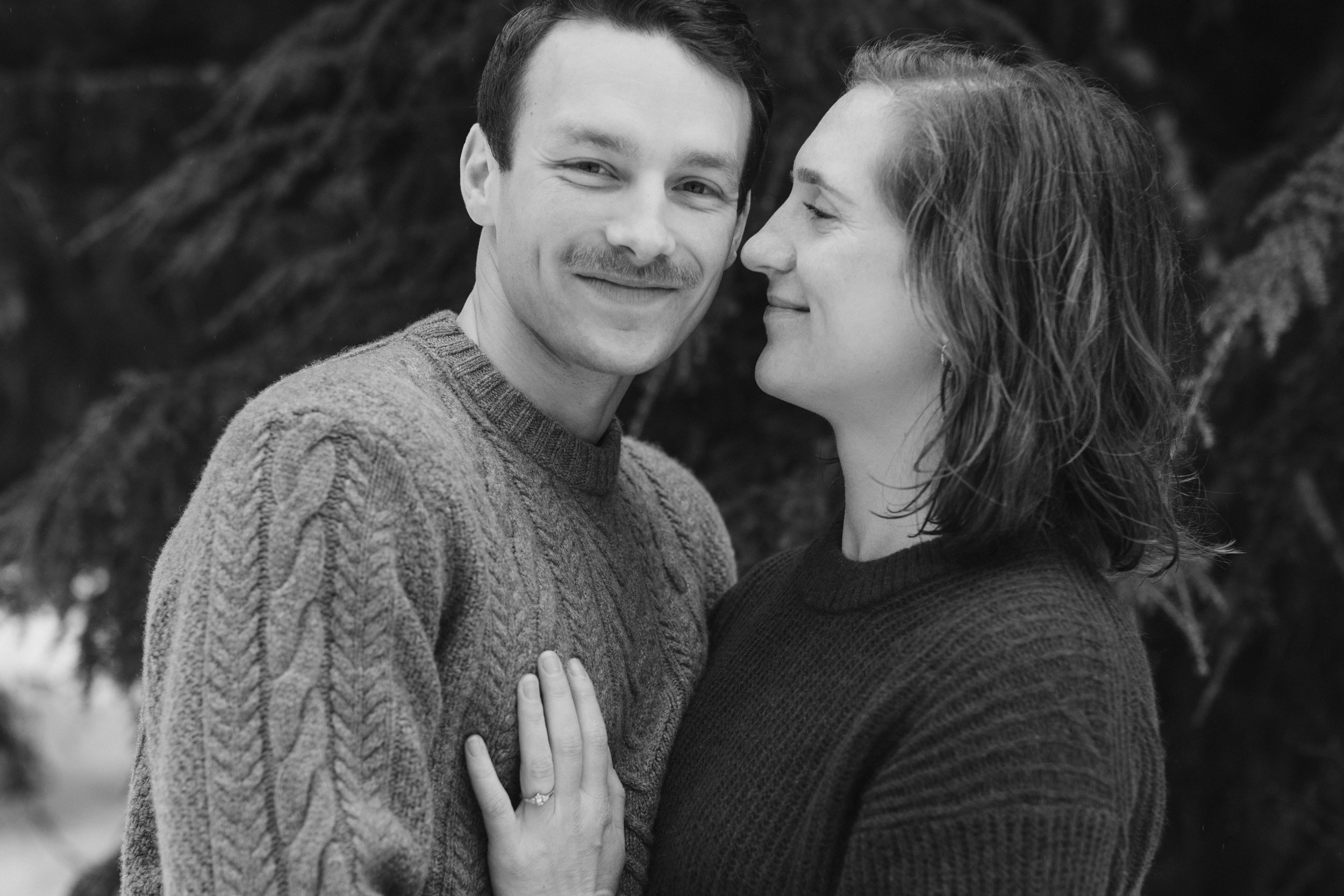 boys looks ahead while girl looks at him, both are wearing sweaters during winter engagement shoot