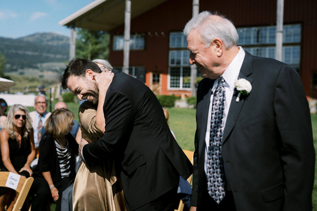 groom hugs parents at end of the aisle