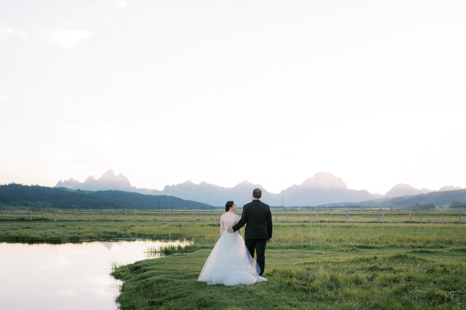 bride and groom standing in field looking out towards mountains